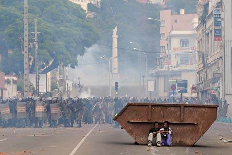Deux partisans d’Andry Rajoelina, maire d’Antananarivo, se tenant derrière une benne, à l’abri des tirs de gaz lacrymogène des f